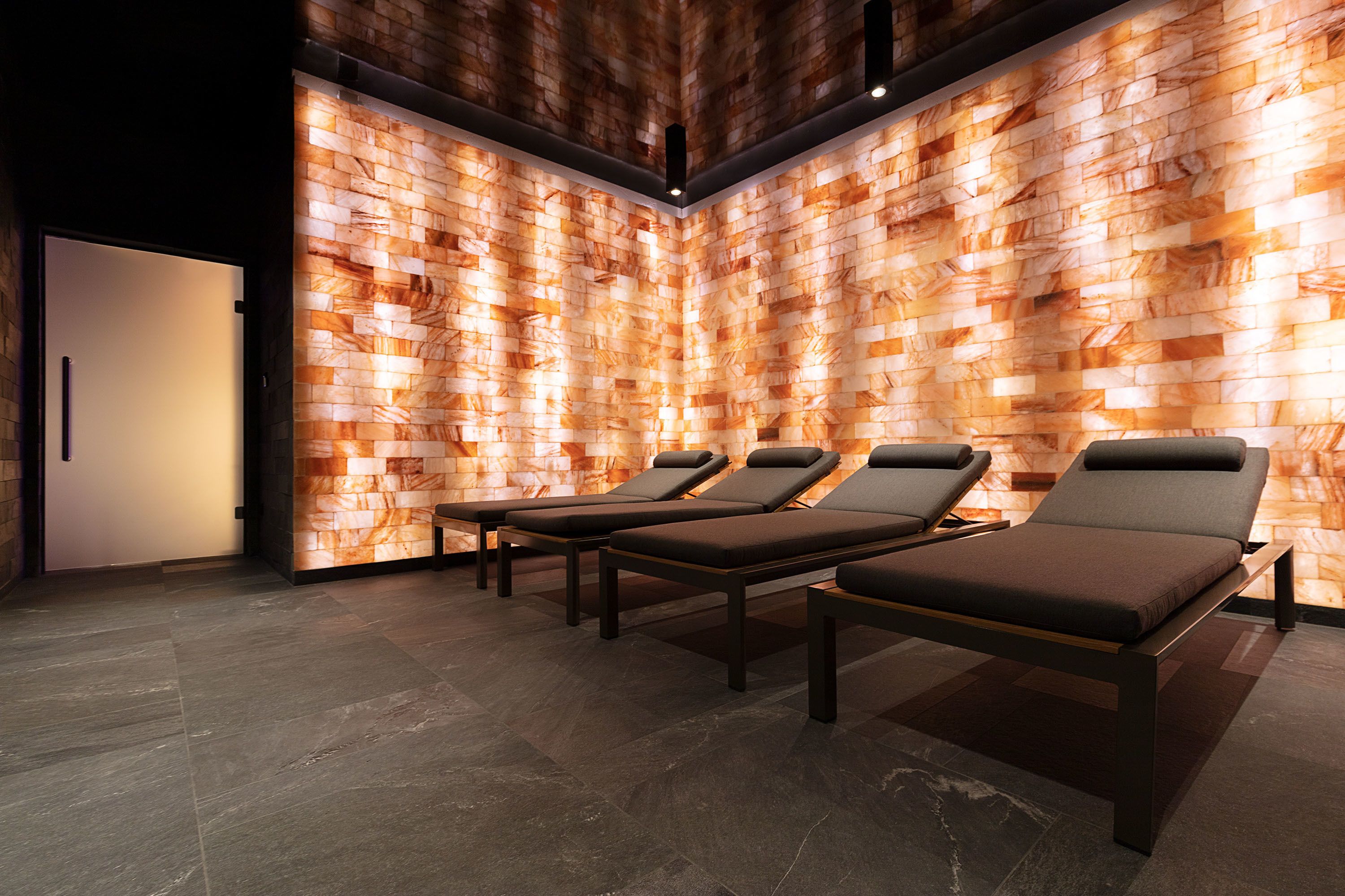 Ein Spa-Raum mit einer Holzvertäfelung, drei Liegen und einer Tür.