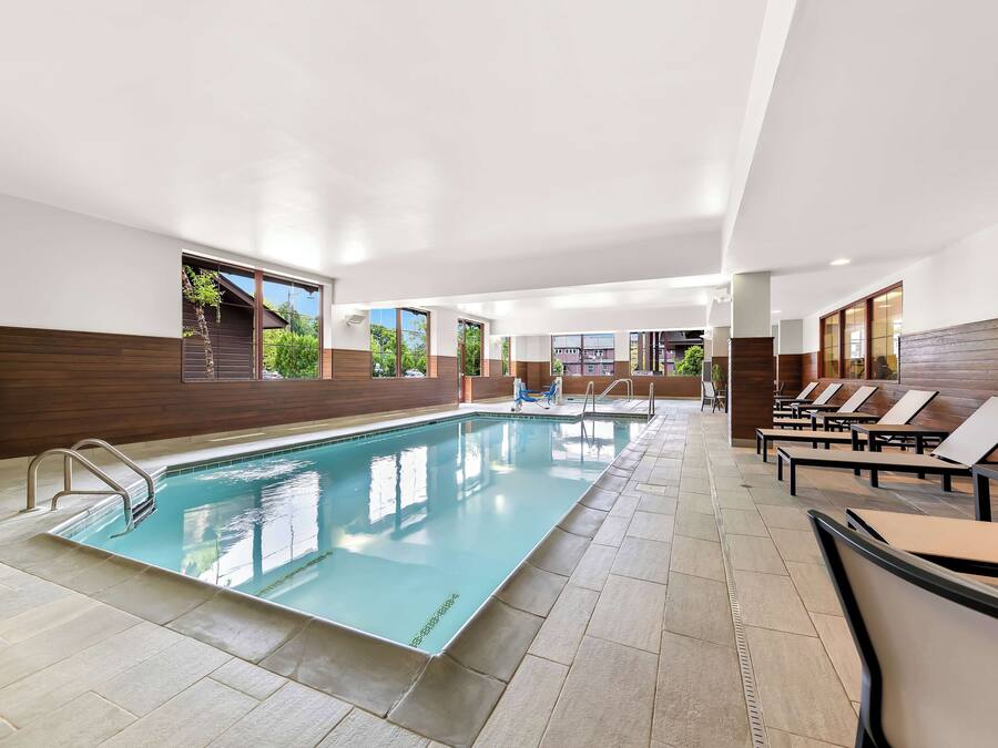 An indoor swimming pool with clear water, surrounded by lounge chairs and a wooden wall.
