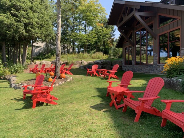 A patio with red Adirondack chairs and a stone fireplace surrounded by a natural landscape.