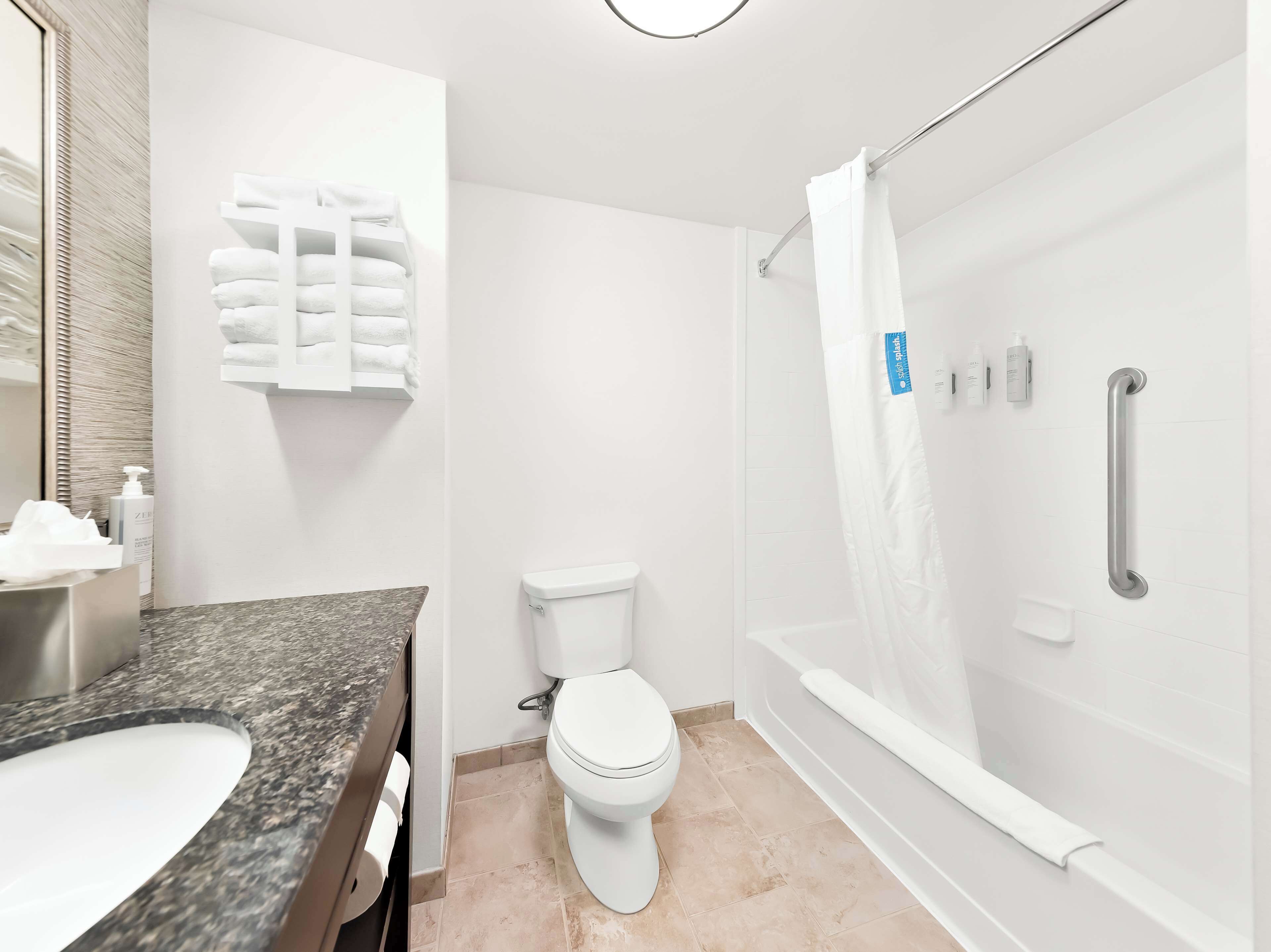 Une salle de bain moderne avec un comptoir en granit, des toilettes blanches et une douche à l’italienne dotée d’une porte en verre.