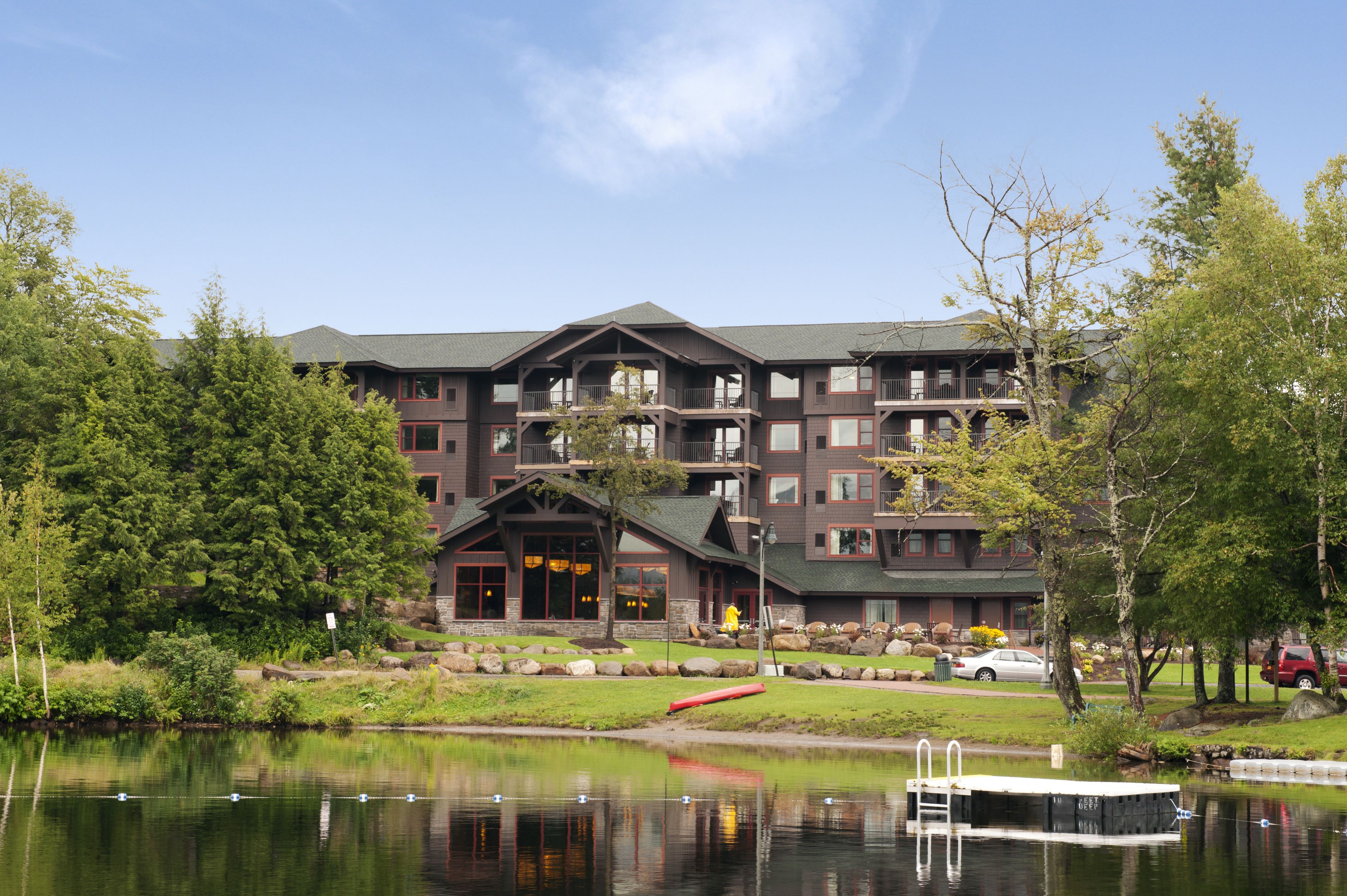 A multi-story hotel with a large entrance, a dock, and a lake in front.