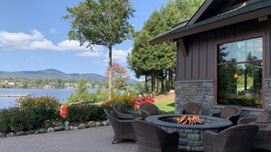 A patio area with wicker furniture and a stone fire pit, overlooking a lake and mountains. - Hampton Inn & Suites Lake Placid (Lake Placid)