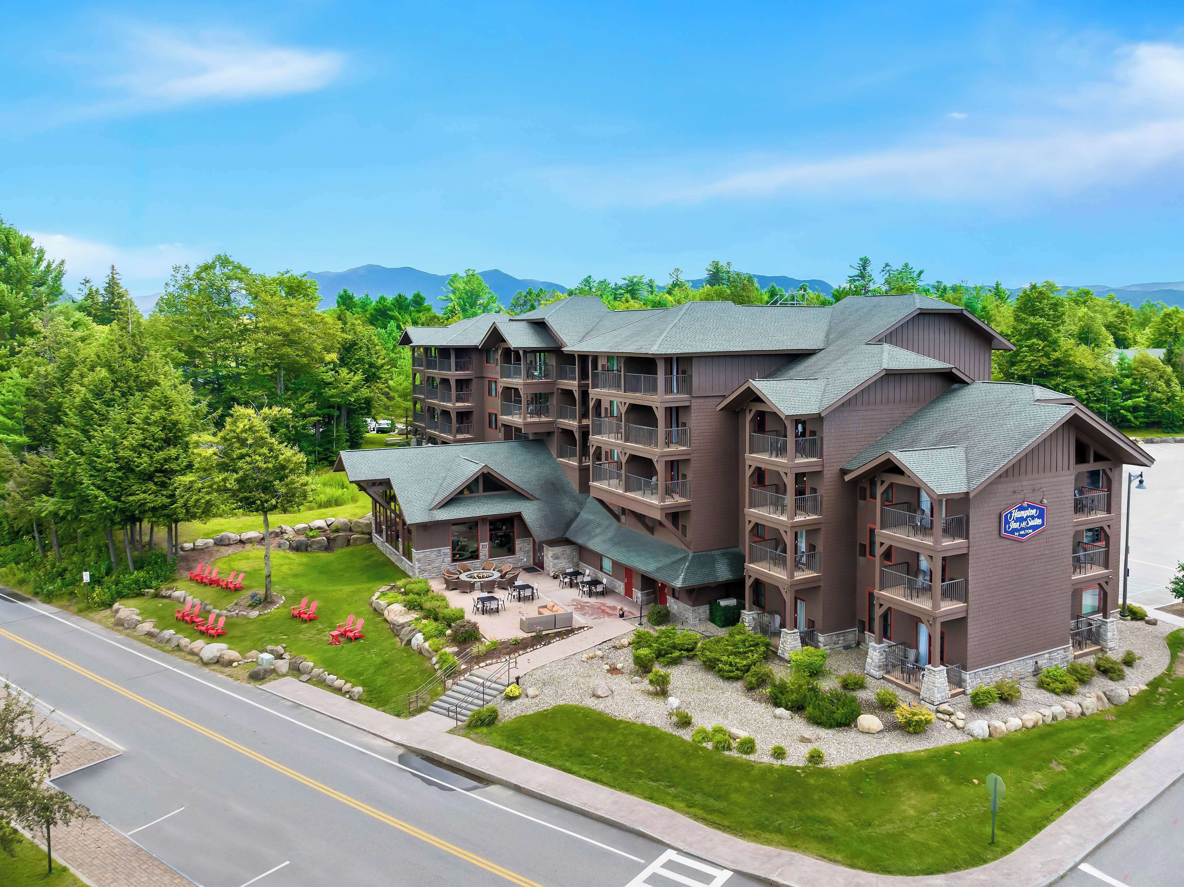 Un hotel de varios pisos con fachada de piedra, zona de estar al aire libre y un cartel que indica que es un establecimiento Hampton Inn & Suites.