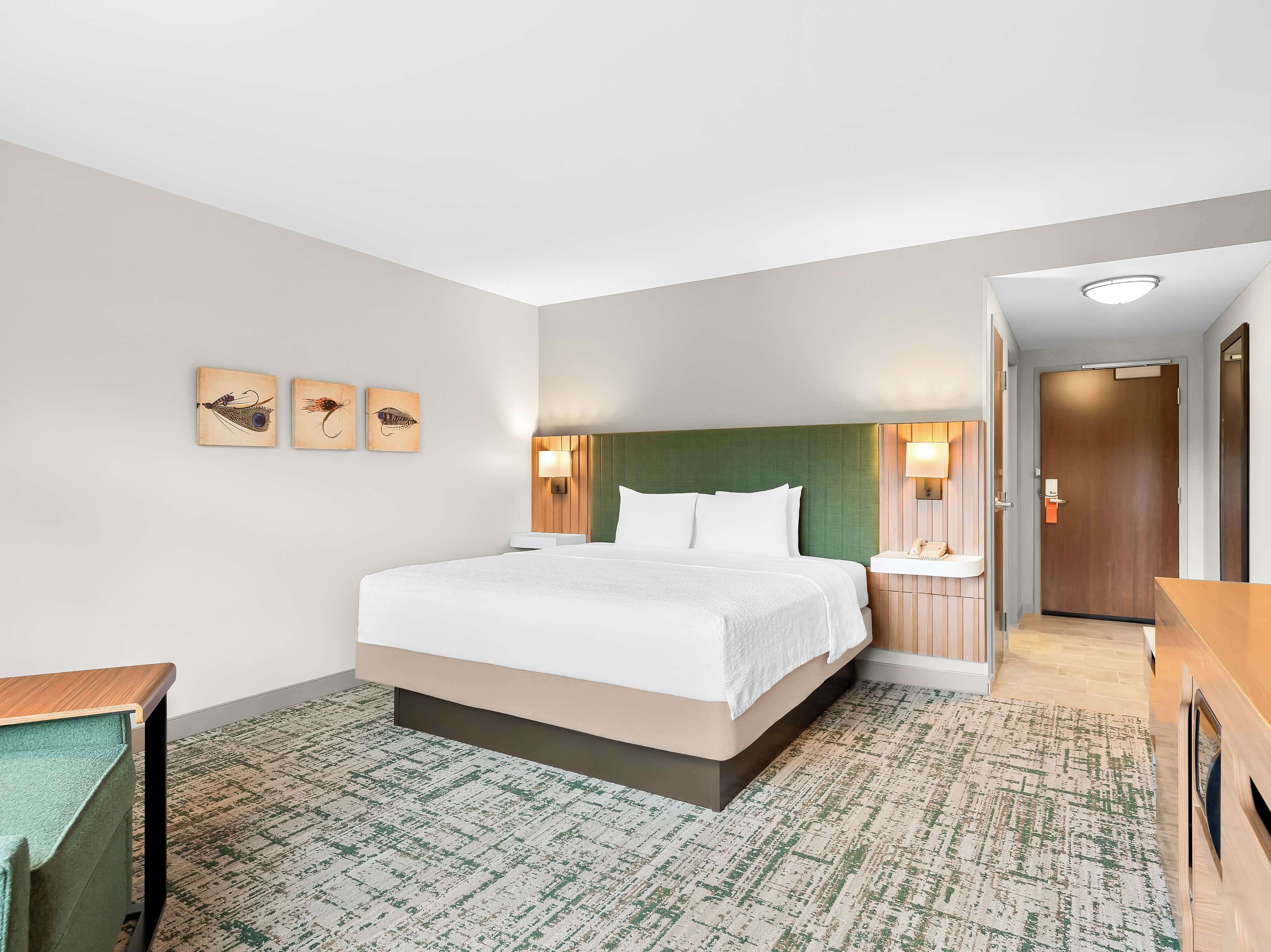 A hotel room with a large bed, a bedside table, a wall-mounted lamp, and a door with a mirror.