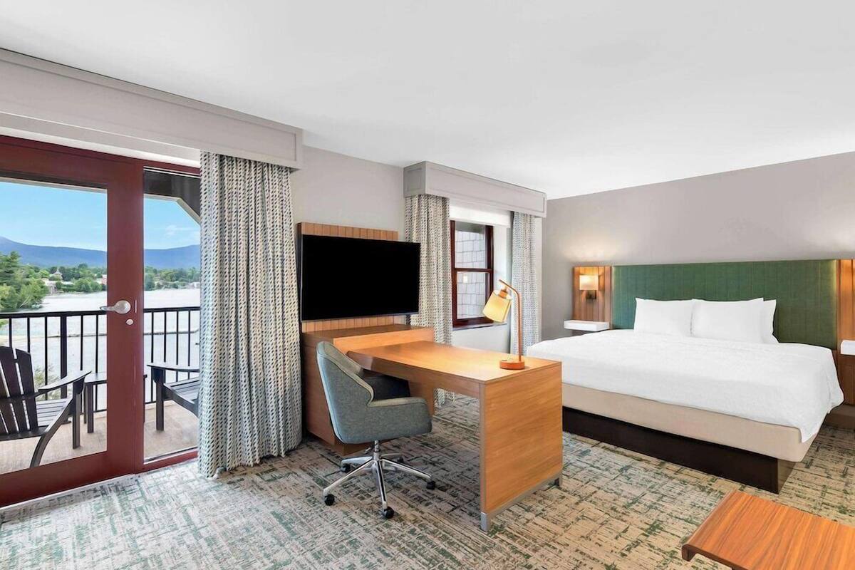 A hotel room with a bed, desk, chair, TV, and a balcony with curtains.