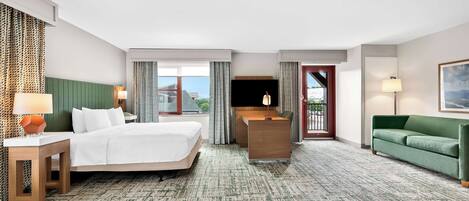 A hotel room with a large bed, a desk, a green sofa, and a TV.