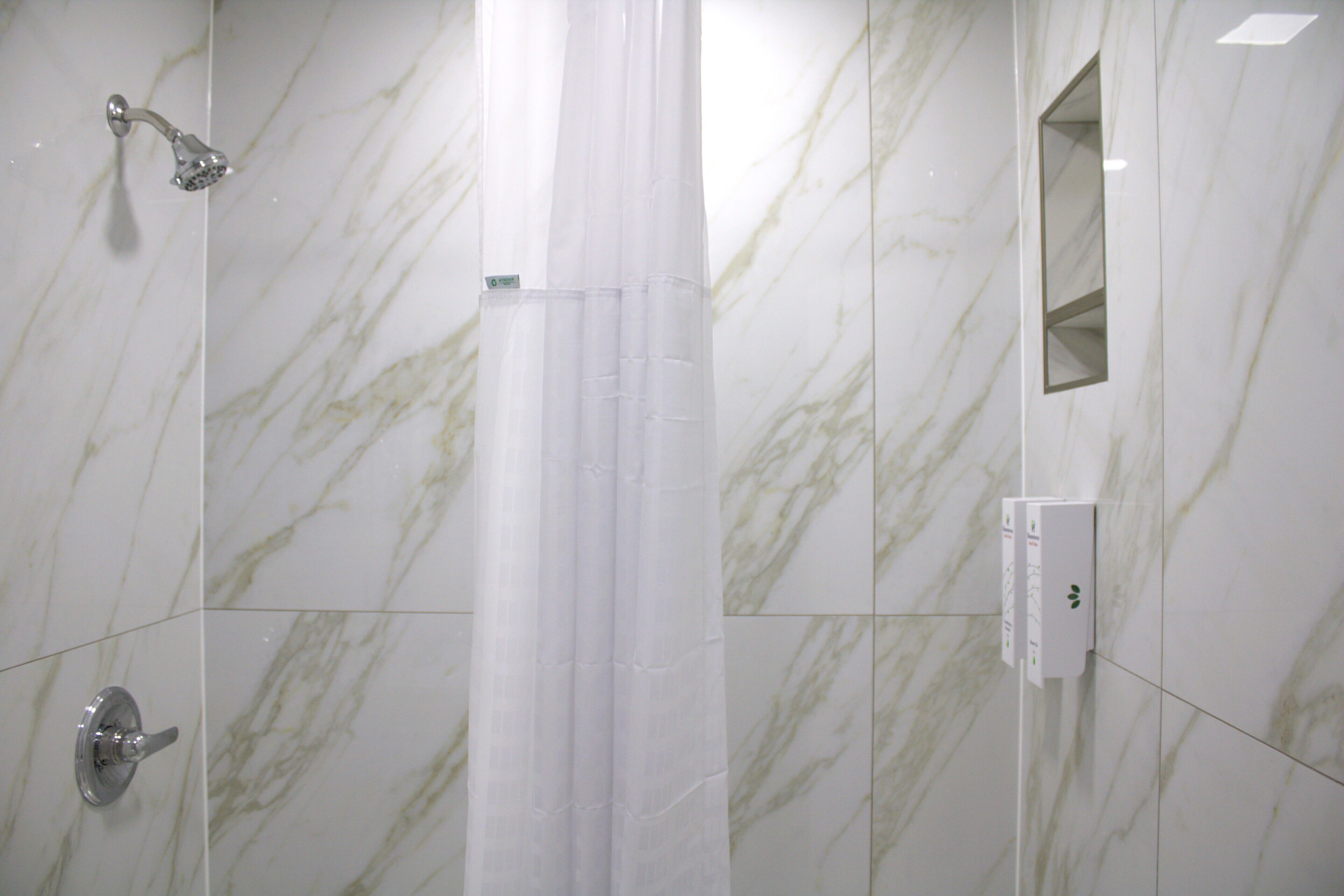 A bathroom with a shower, a toilet, a mirror, and a towel rack.
