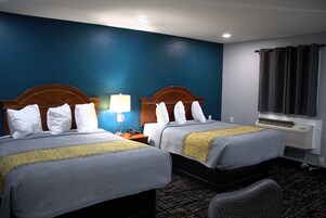 Habitación de hotel con dos camas, una mesita de noche, una lámpara, un equipo de aire acondicionado y una ventana con cortinas.