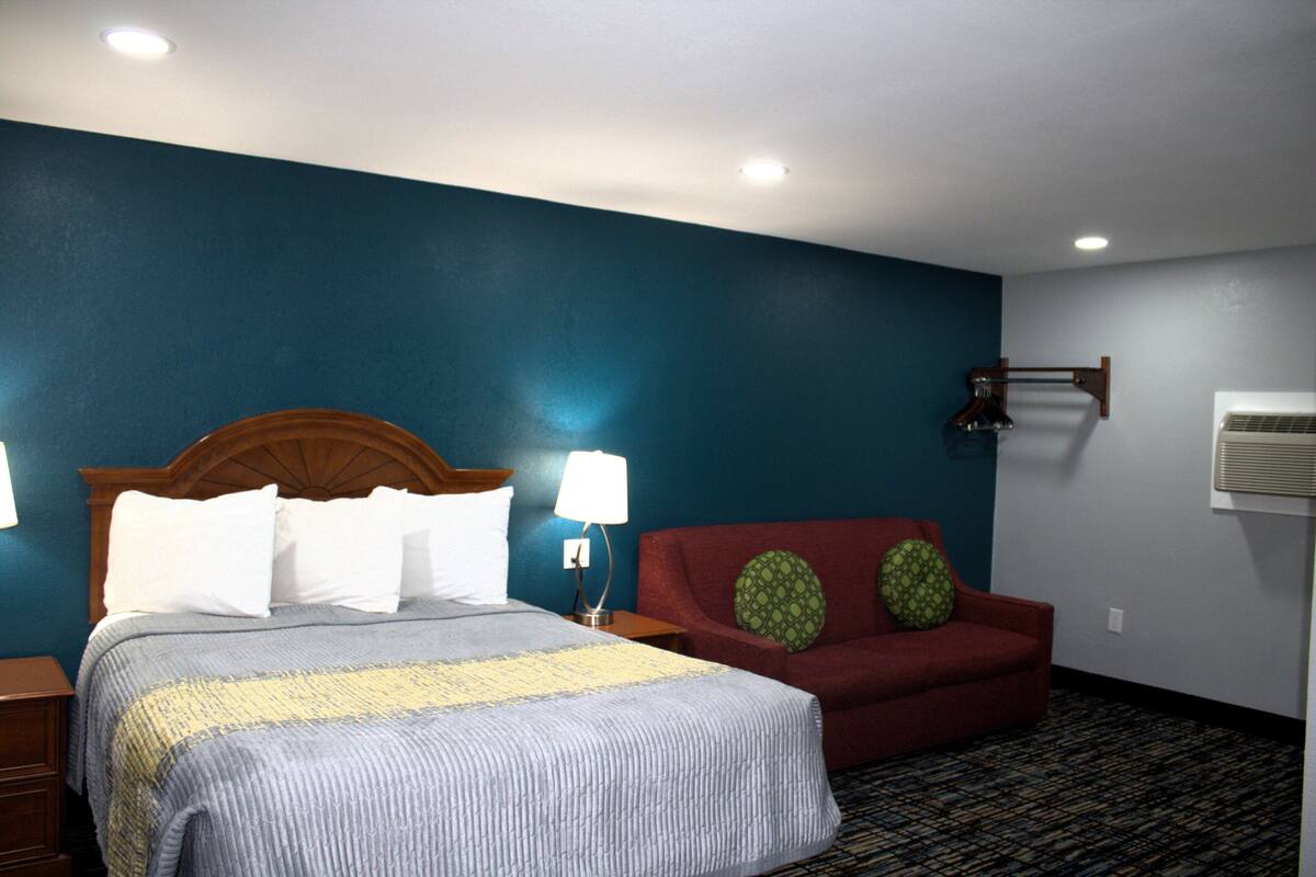 A hotel room with a bed, a red sofa, a patterned carpet, and a wall-mounted air conditioner.