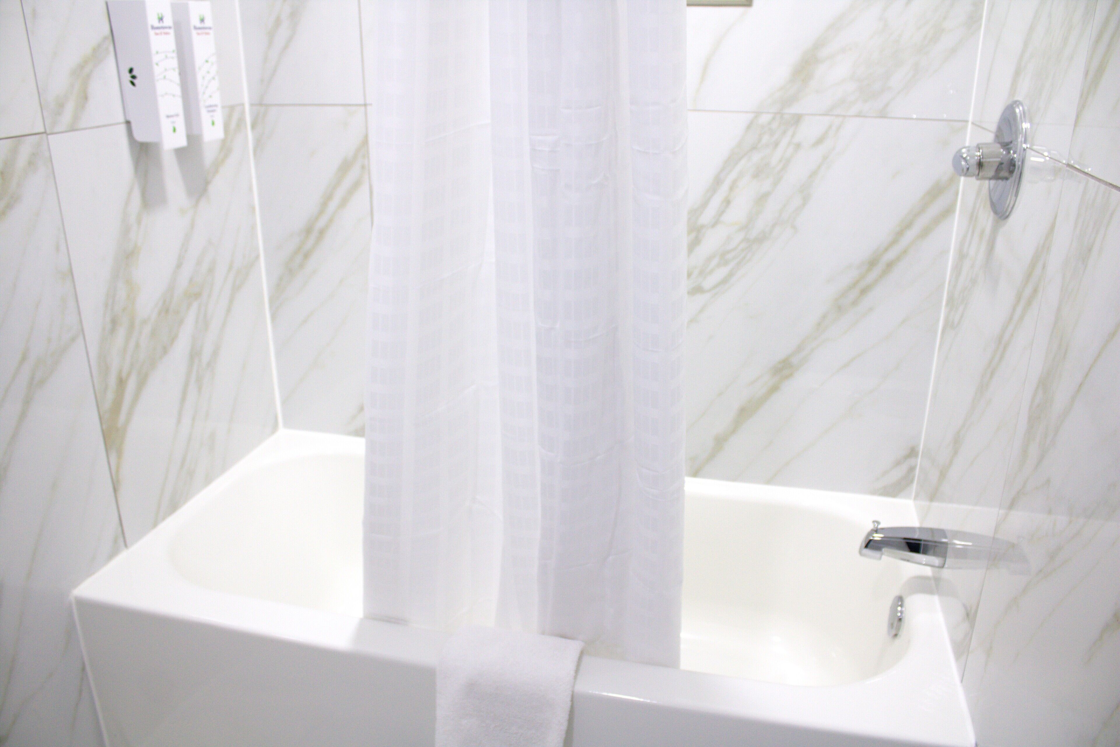 A bathroom with a white bathtub, a shower curtain, and marble tiles.