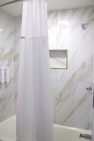 Un baño con cortina de ducha, cabezal de ducha manual y pared con diseño de mármol.