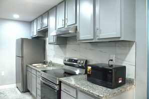 A kitchen with stainless steel appliances, marble countertops, and grey cabinets. - HavenPointe Inn & Suites (Scottsburg)