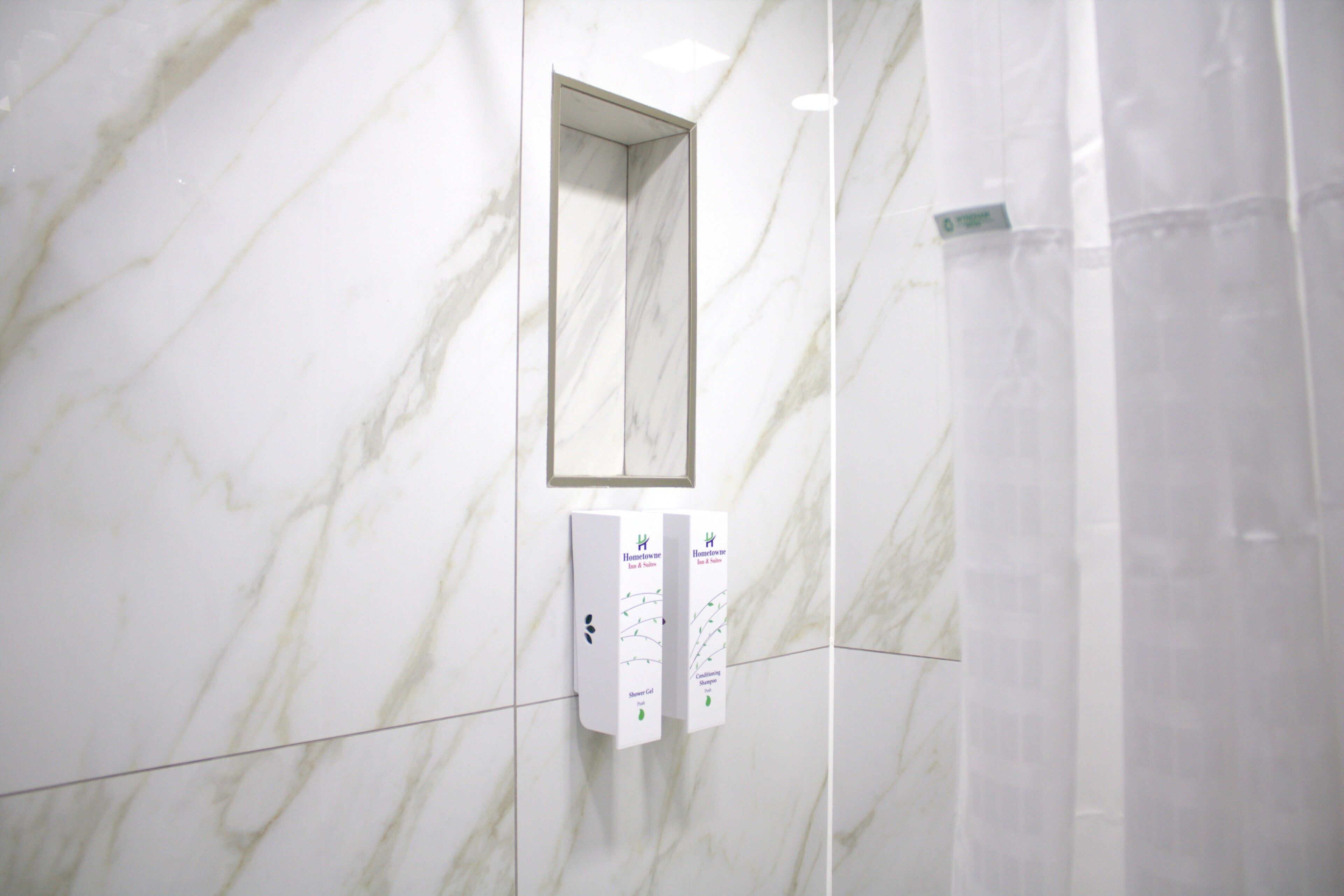 A bathroom with a marble wall, a mirror, and a soap dispenser.