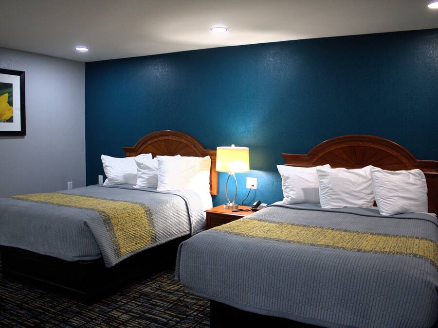 A hotel room with two beds, a nightstand with a lamp, and a framed picture on the wall.