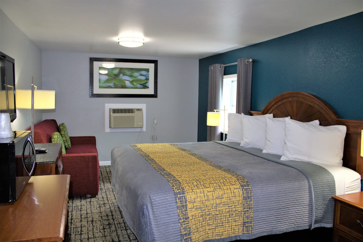 A hotel room with a bed, a desk, a chair, a TV, and a framed picture on the wall.