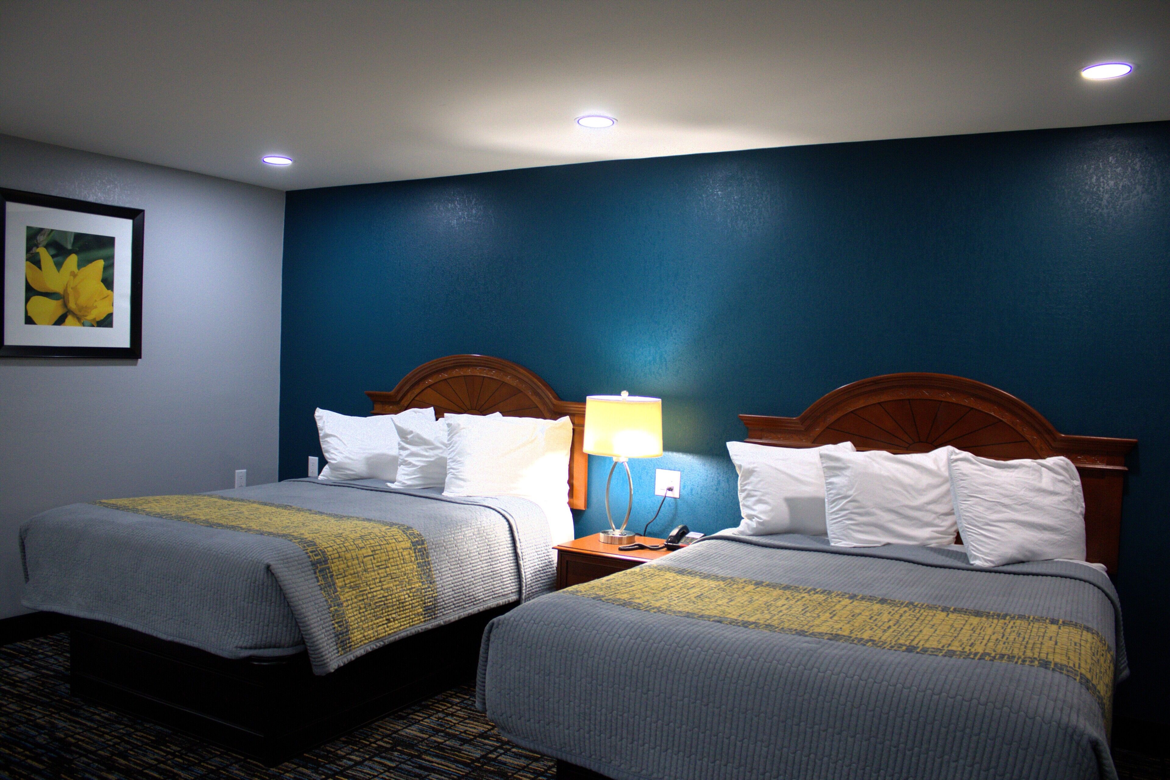 A hotel room with two beds, a nightstand with a lamp, and a framed picture on the wall.