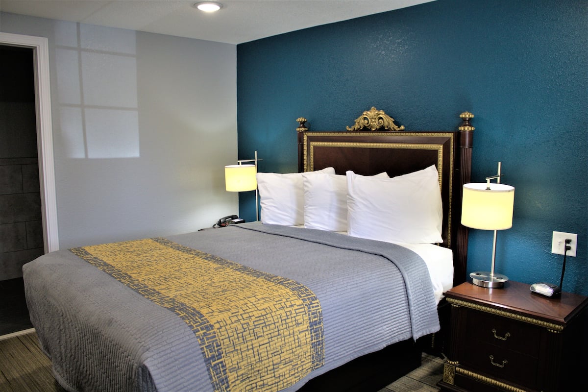 A hotel room with a large bed, two bedside tables with lamps, a nightstand, and a wall-mounted telephone.