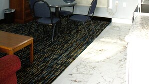 Une pièce dotée d’un téléviseur à écran plat fixé au mur, d’une table à manger avec des chaises, d’une petite table d’appoint en bois et d’un tapis à motifs.