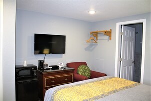 Habitación de hotel con cama, televisor montado en la pared, microondas, cómoda pequeña y una puerta.