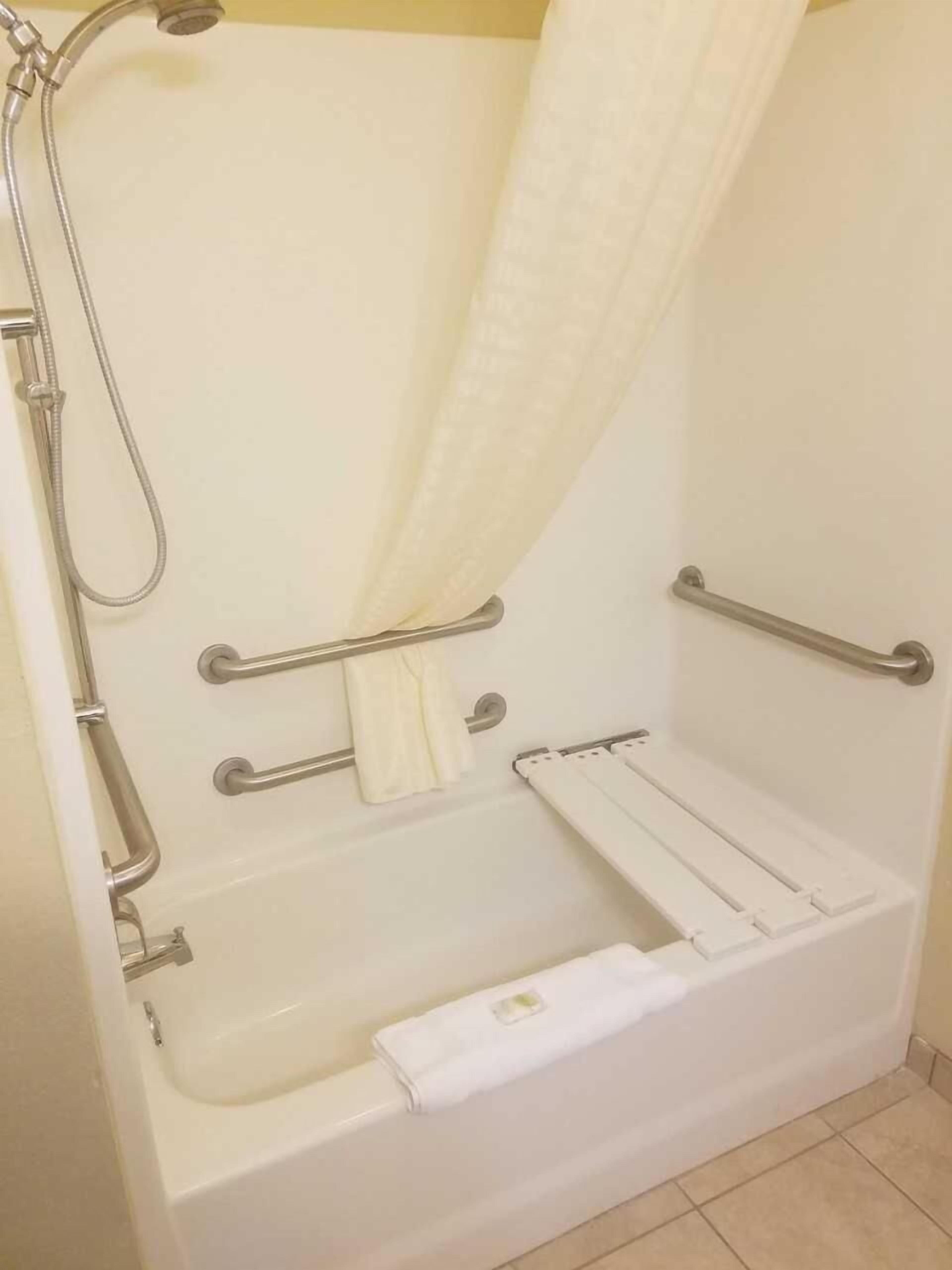 A white bathtub with a shower head, grab bars, and a towel rack.