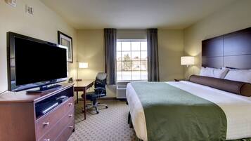 Una habitación de hotel con cama, escritorio, televisor y ventana con cortinas.