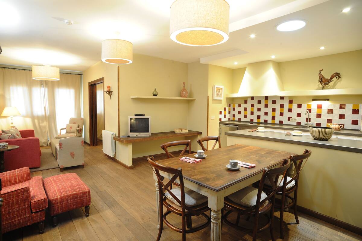 A cozy living room with a red sofa, a wooden dining table with four chairs, and a television on a stand.
