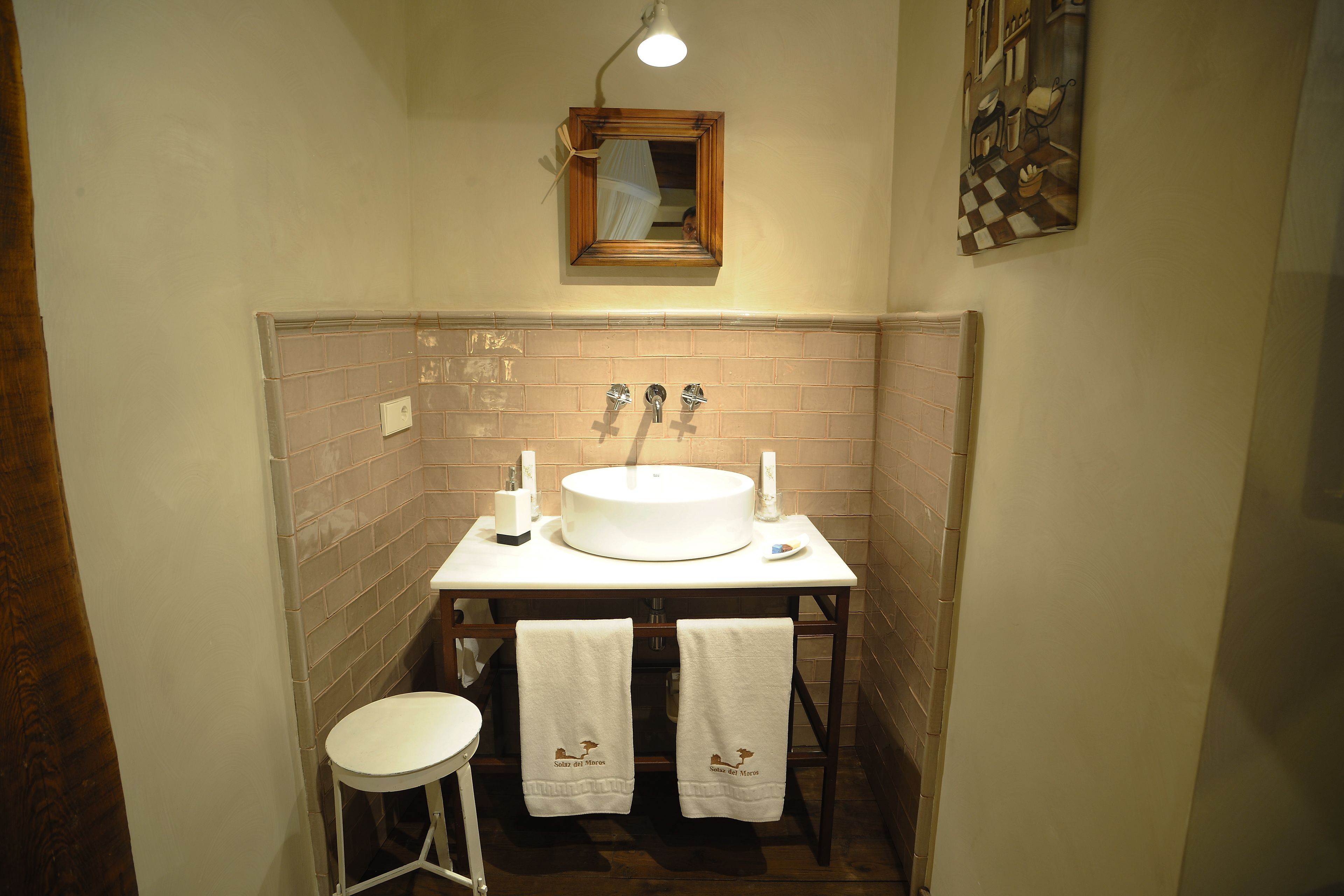 A bathroom with a round sink, two towel racks with towels, a mirror, and a light fixture.