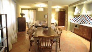 Un coin repas avec une table et des chaises en bois, une cuisine avec un dosseret à carreaux et un salon avec un canapé et des rideaux.