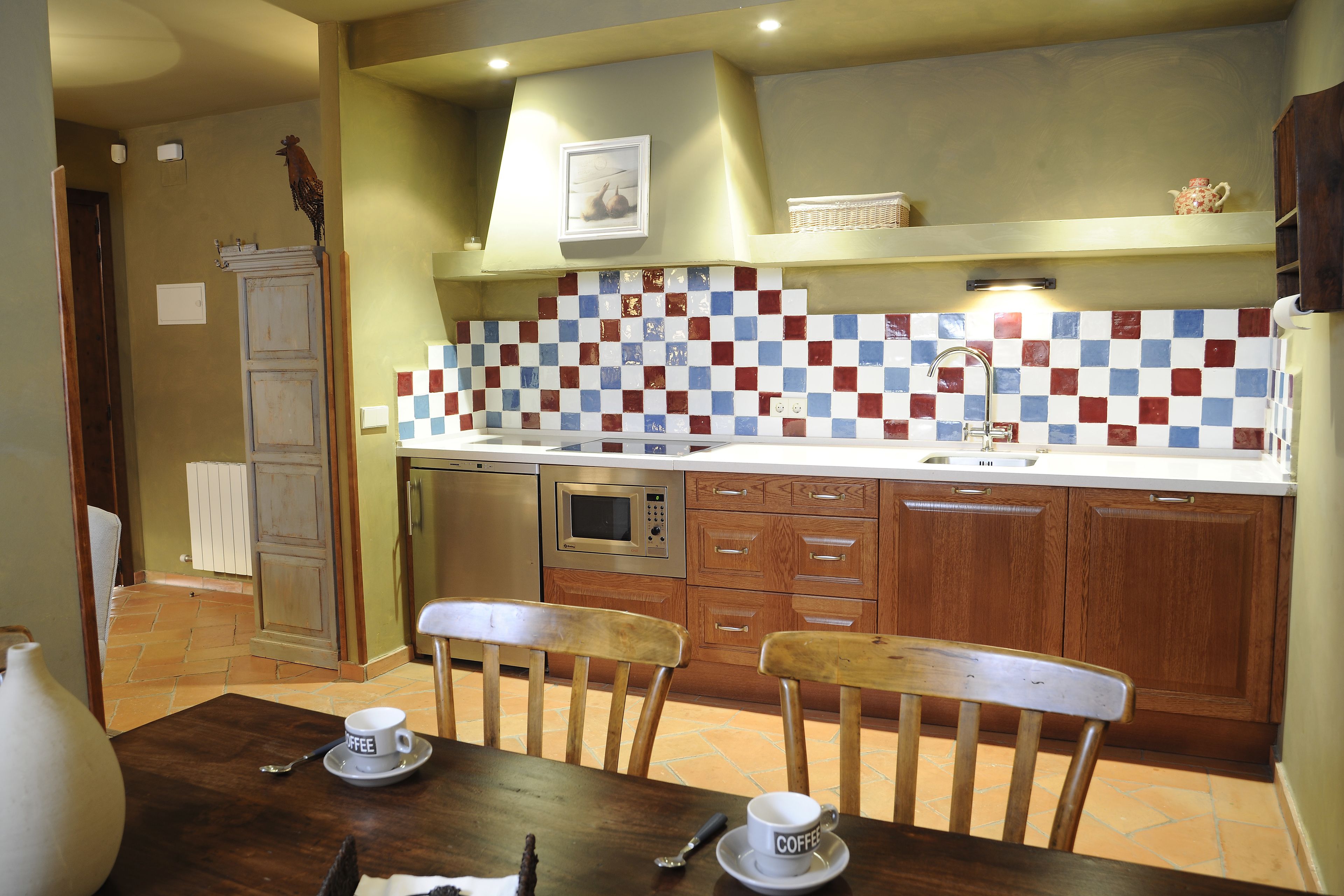 A kitchen with a tiled backsplash, wooden cabinets, a microwave, and a dining area with chairs and a table.