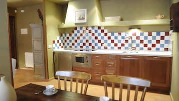 A kitchen with a tiled backsplash, wooden cabinets, a microwave, and a dining area with chairs and a table.