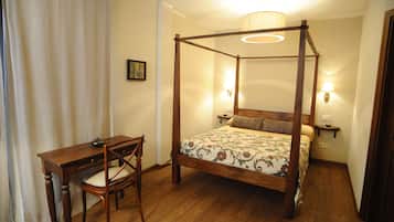 Un lit à baldaquin avec une couvre-lit à motifs floraux, un bureau en bois avec une chaise et deux lampes fixées au mur.