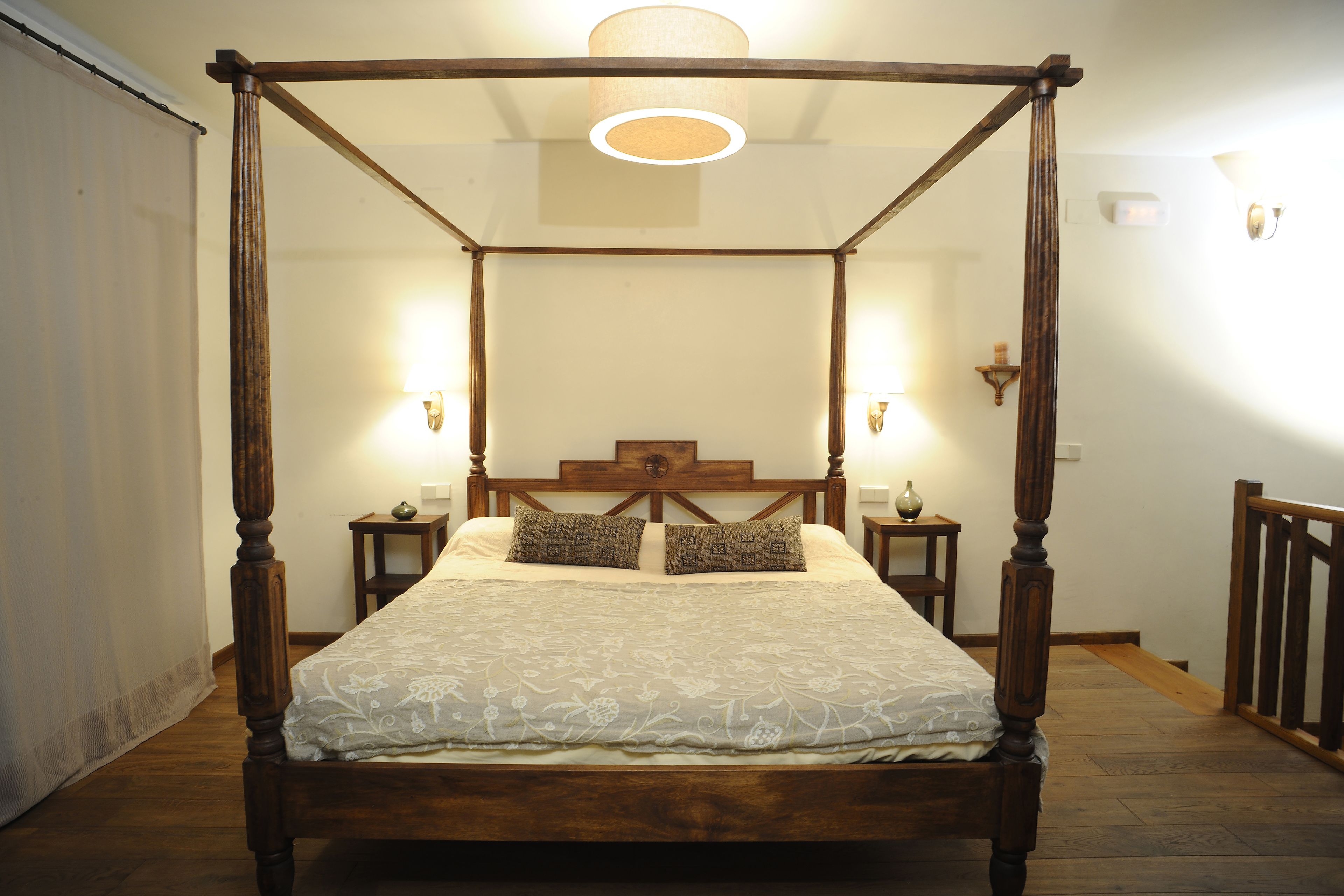 Una cama con dosel, dos mesitas de noche y lámparas fijadas a la pared.