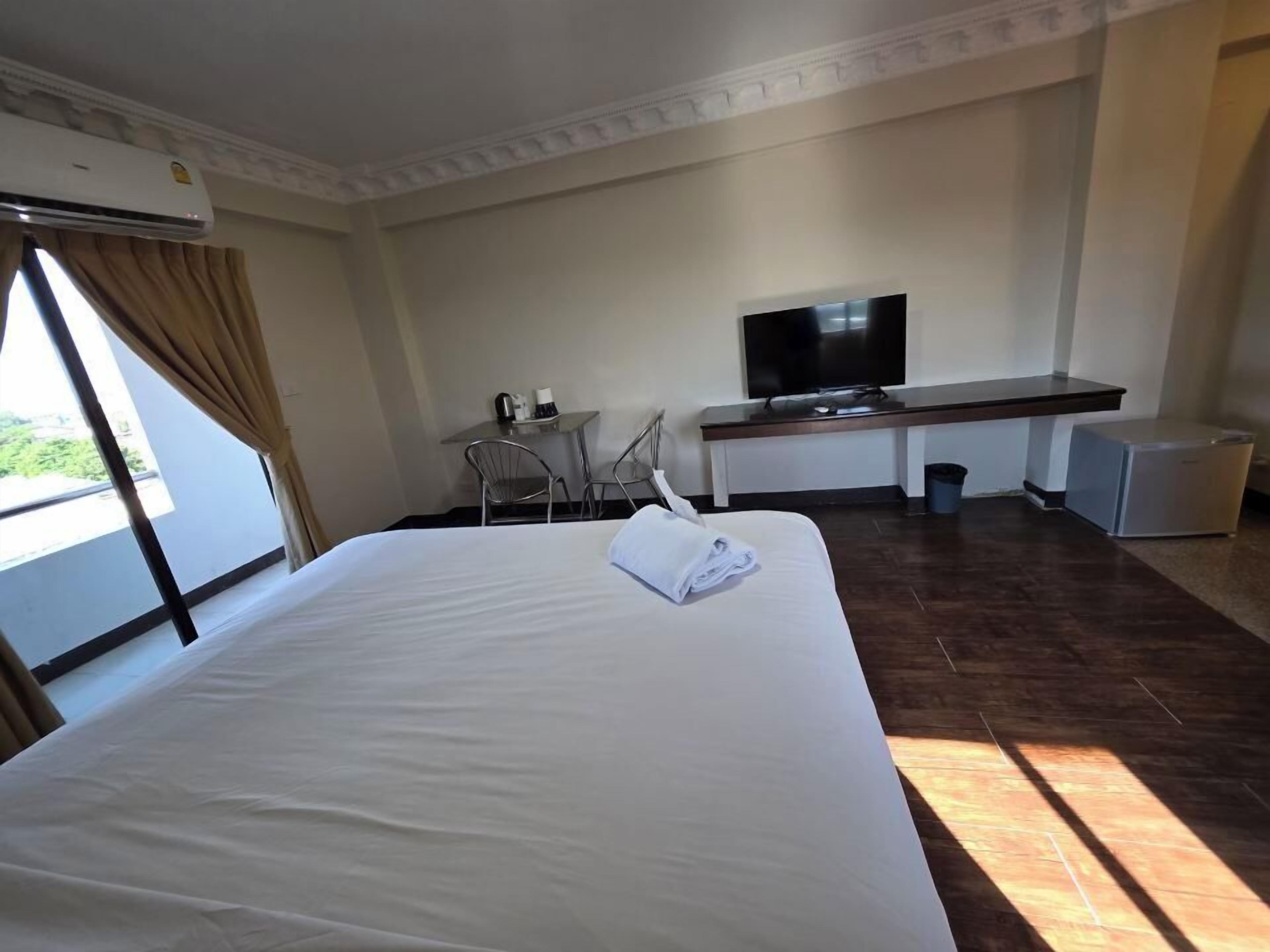 A hotel room with a large bed, a desk with a television, a small refrigerator, and a window with curtains.