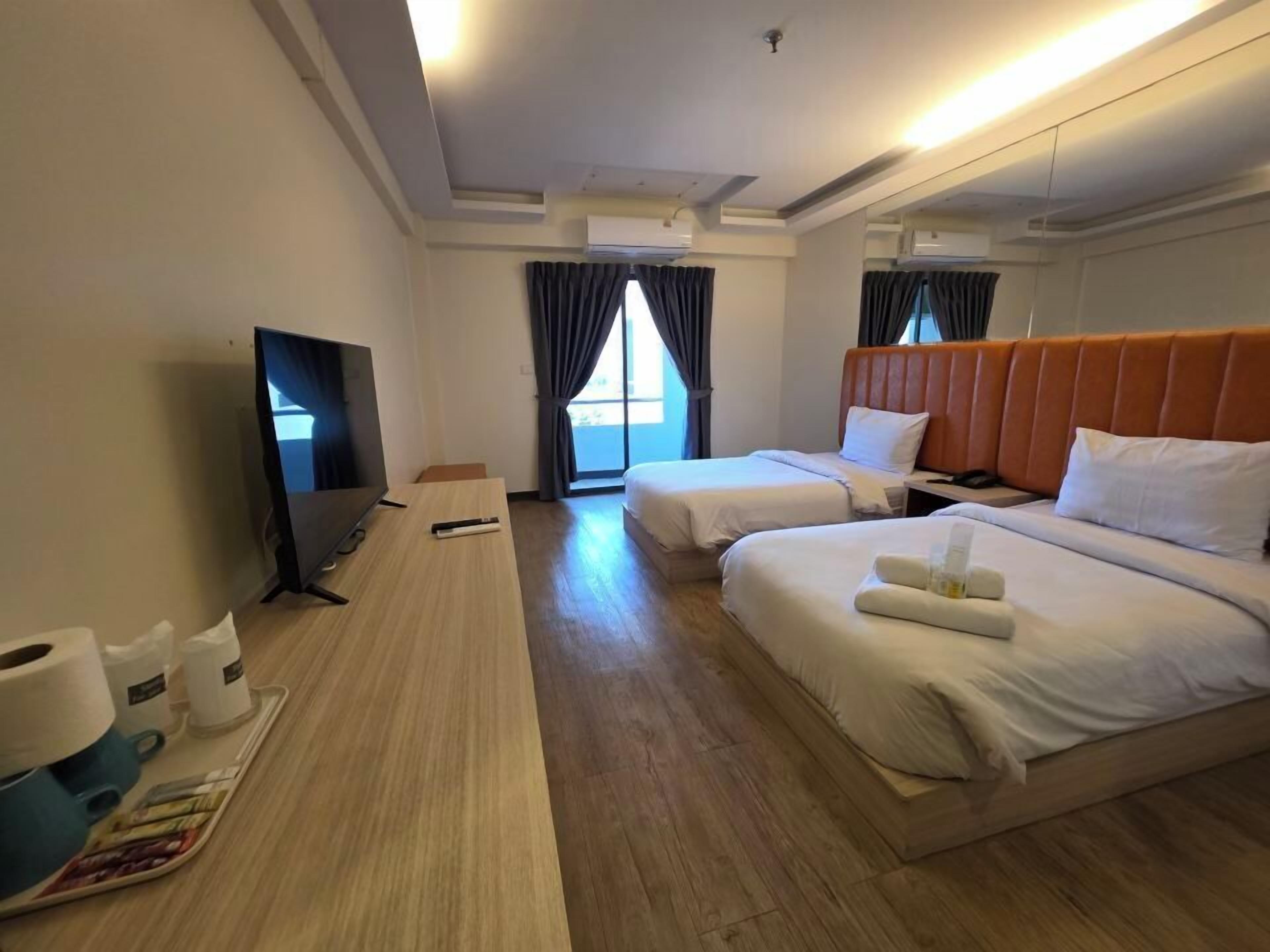 Quarto de hotel com duas camas, televisão, escrivaninha com computador e janela com cortinas.