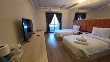 Quarto de hotel com duas camas, televisão, escrivaninha com computador e janela com cortinas.