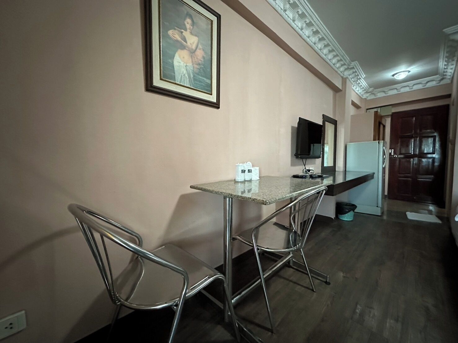 A small kitchen with a table and two chairs, a refrigerator, a television, and a framed picture on the wall.