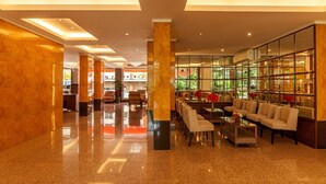 A spacious lobby with a polished floor, a seating area with sofas and chairs, and a large window with a view of greenery. - Tara Lake Hotel (Bangkok)