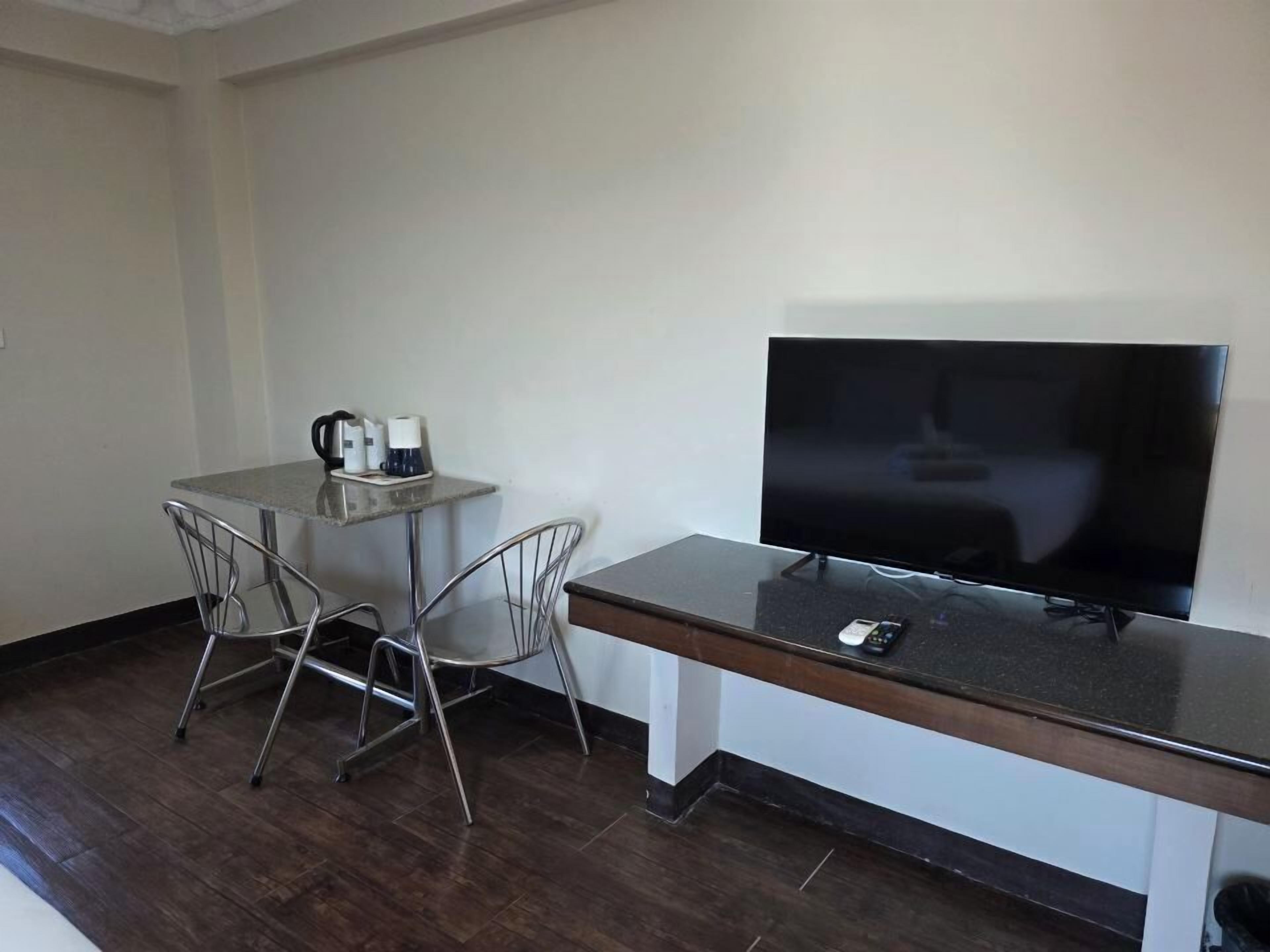 Una habitación pequeña con televisión, cafetera y dos sillas.