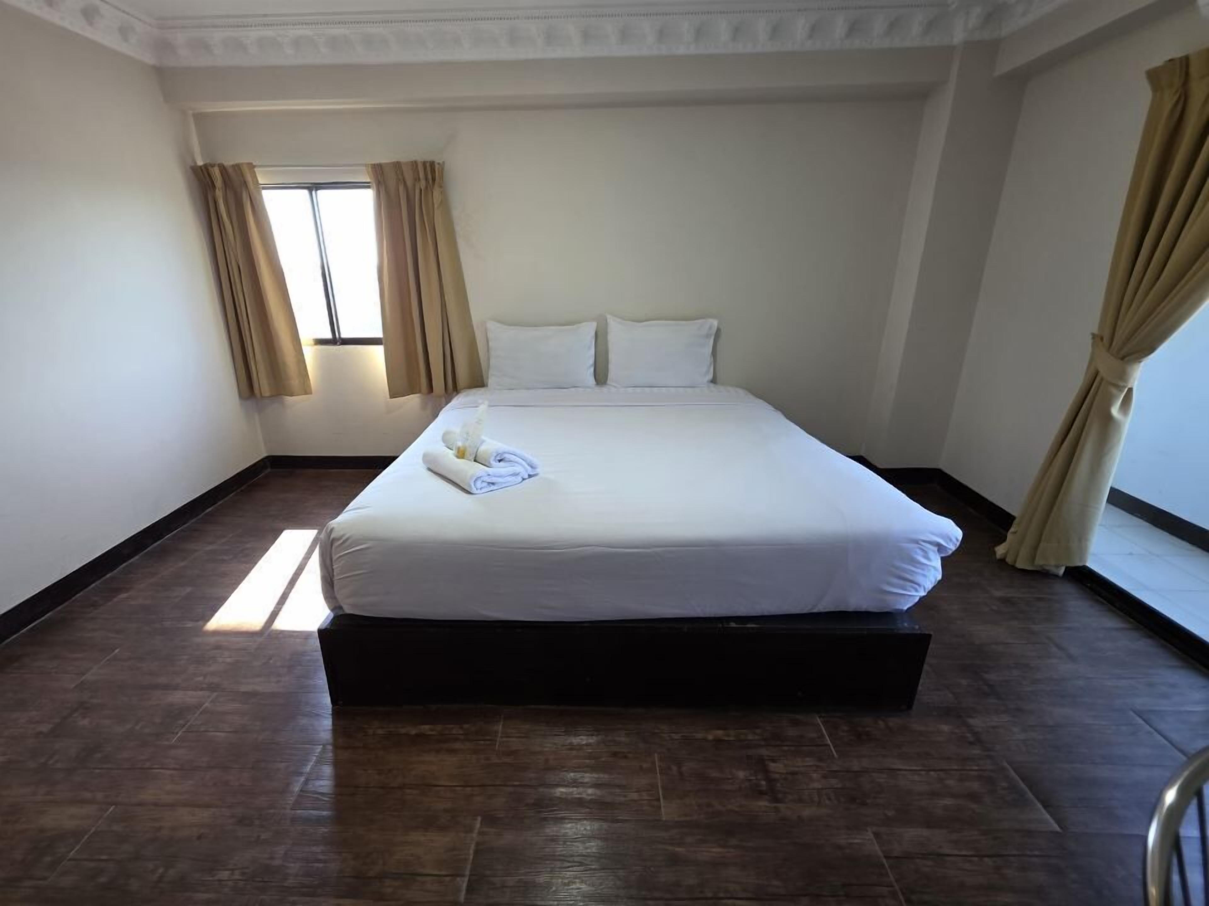 Habitació d'hotel amb un llit gran, cortines beix i un terra de fusta.