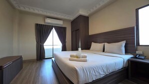 A hotel room with a large bed, a bedside table, an air conditioning unit, and a window with curtains. - Tara Lake Hotel (Bangkok)