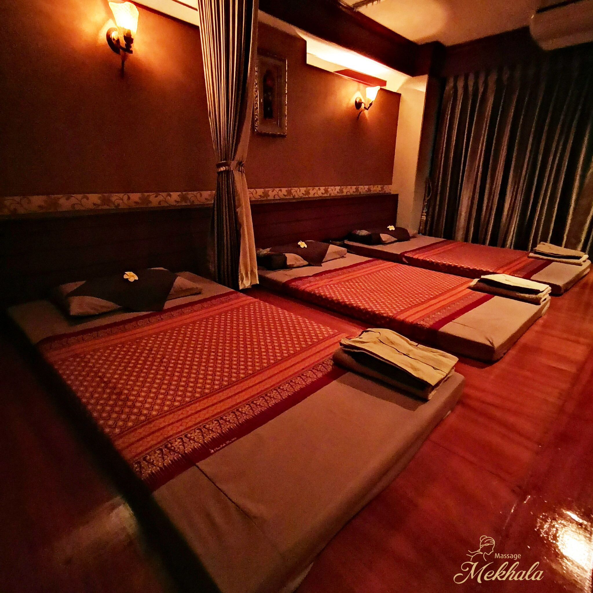 A massage room with four beds, each with a red mat and a towel.