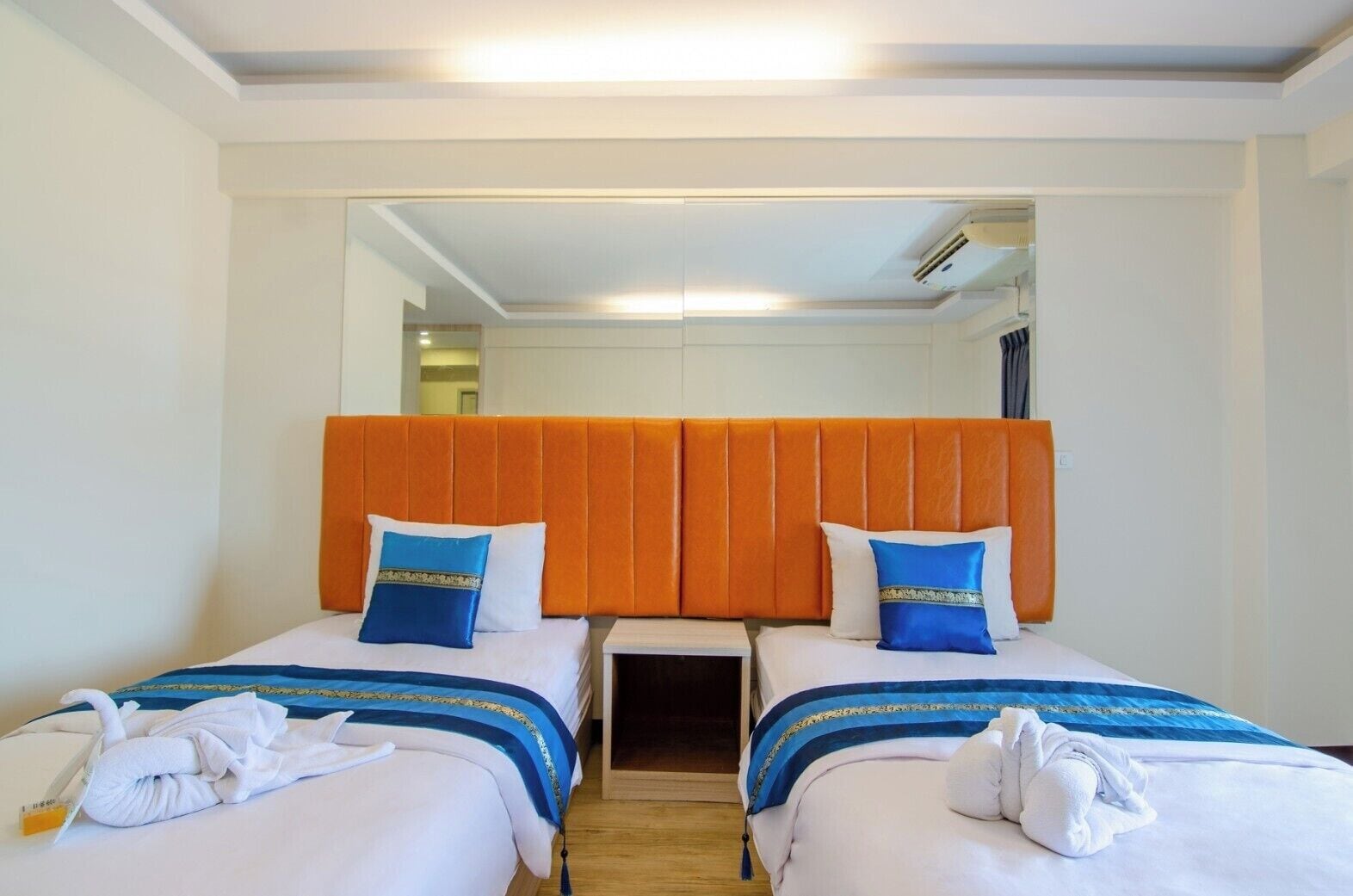 A hotel room with two beds, each with a blue and white bedspread, orange headboards, and matching pillows.