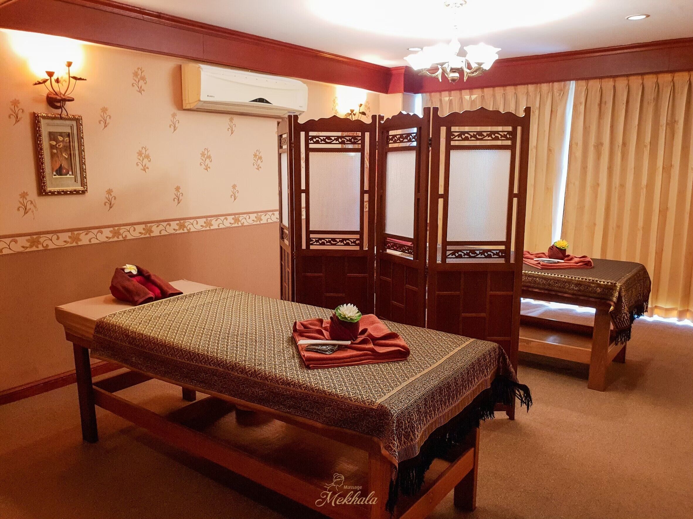 A traditional massage room with a wooden bed, a massage table, a wall-mounted air conditioner, and a decorative mirror.