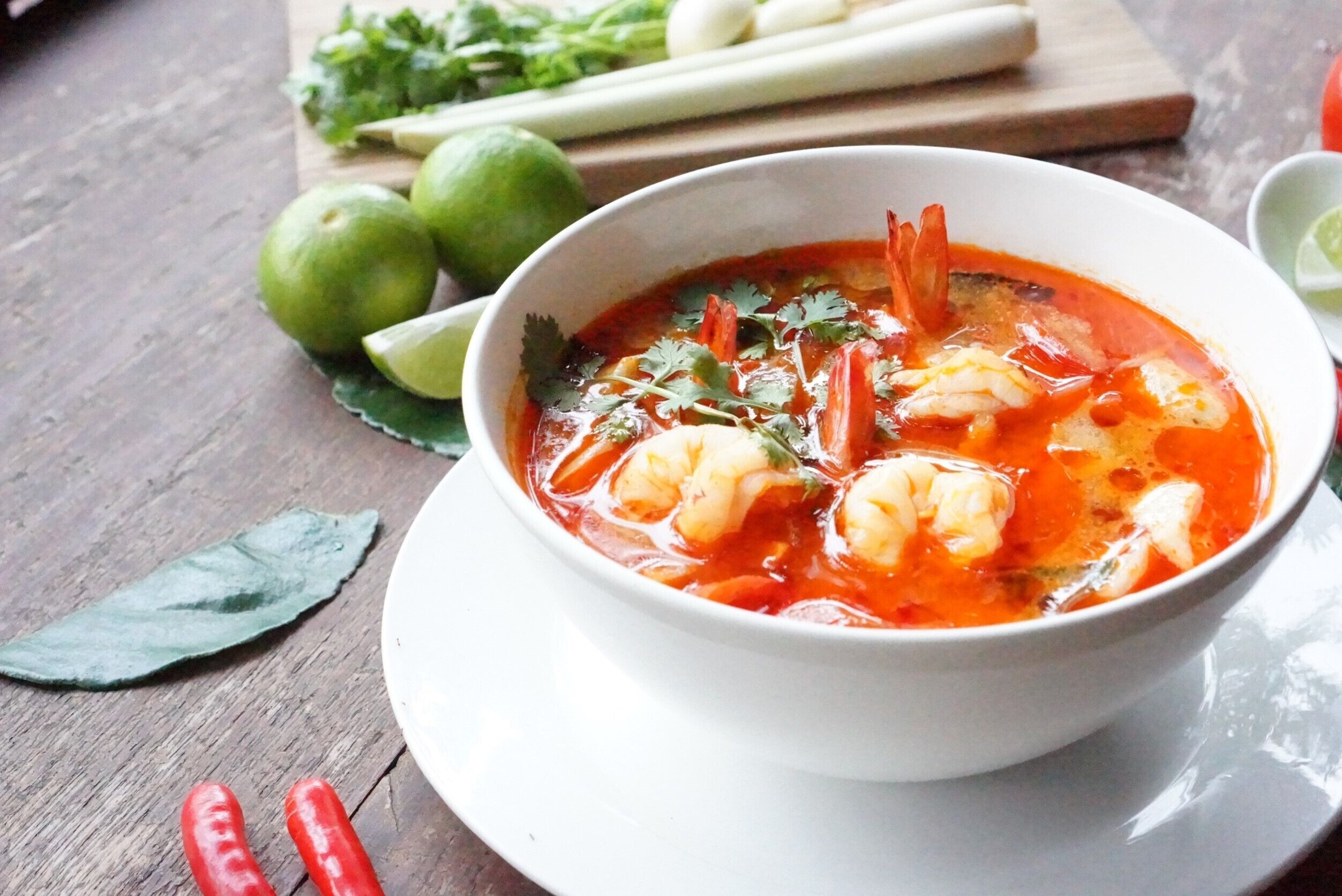 Un bol de soupe aux crevettes, garni de coriandre, servi dans une assiette blanche.