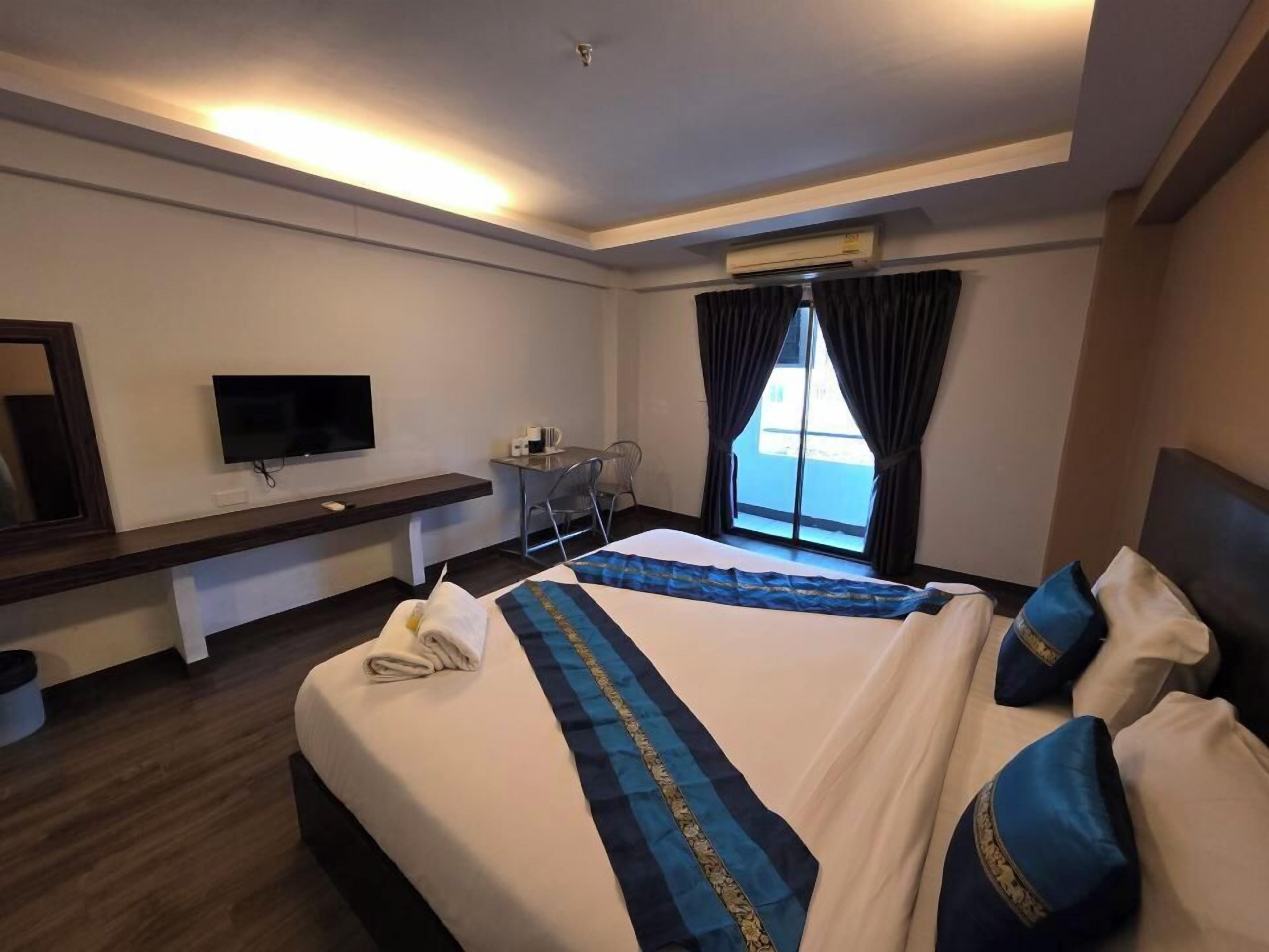 Une chambre d’hôtel équipée d’un lit, d’un bureau, d’une chaise, d’une télévision et d’une fenêtre avec des rideaux.