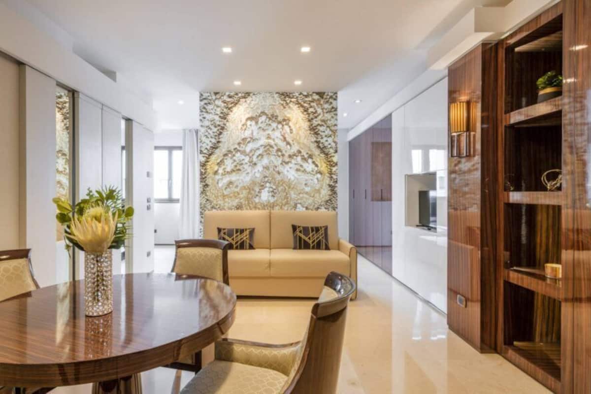 Un interior moderno con una mesa de comedor redonda, sofá beige y una pared decorativa.