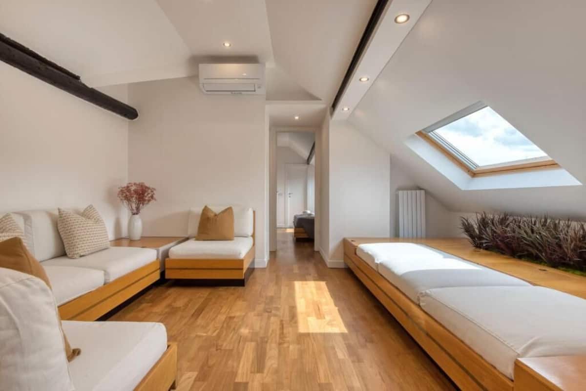 Un dormitorio tipo loft moderno con tragaluces, suelo de madera y una zona de estar central.