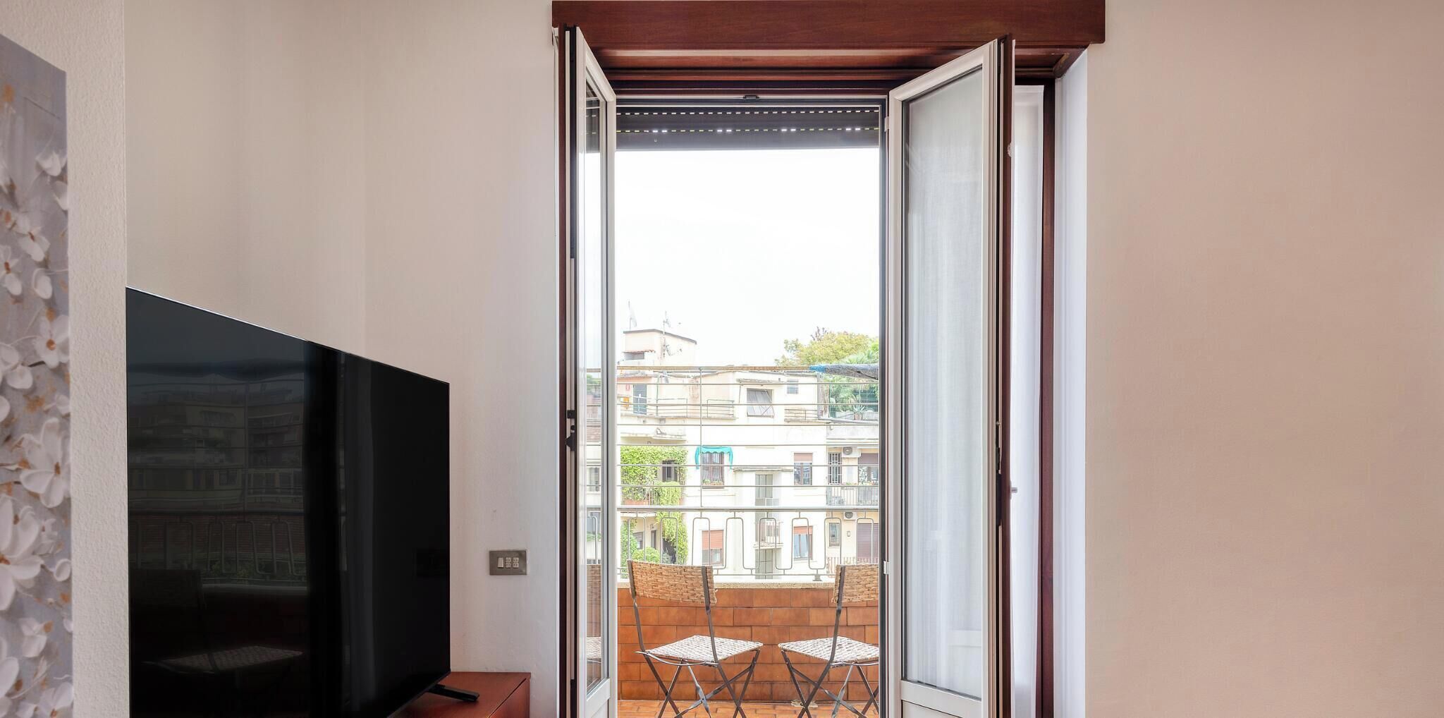 Ein Zimmer mit Fernseher, eine Glasschiebetür zu einem Außenbereich mit Tisch und Stühlen.