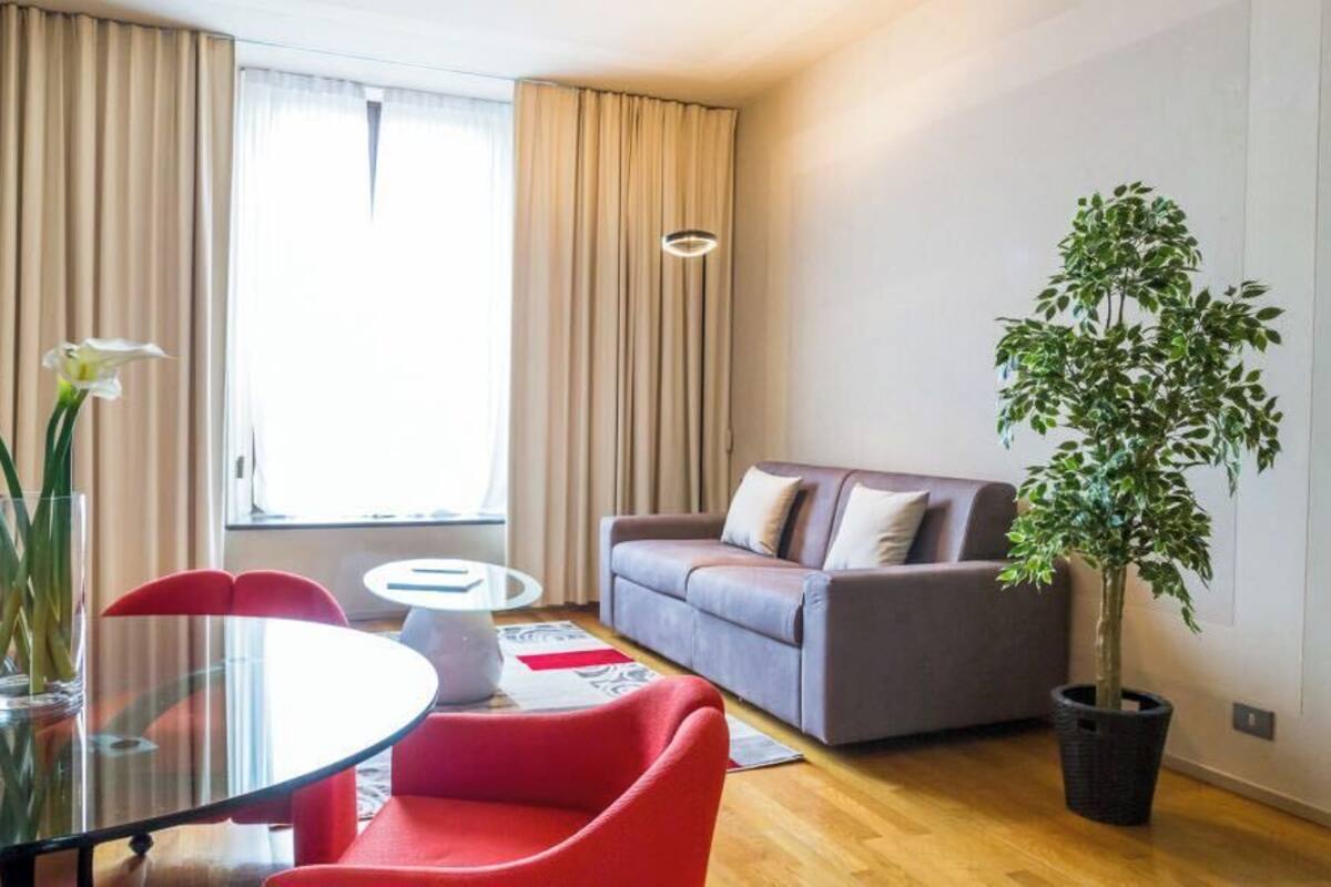 Una sala de estar moderna con una mesa de comedor de vidrio, sillas rojas, un sofá gris y una planta en maceta.