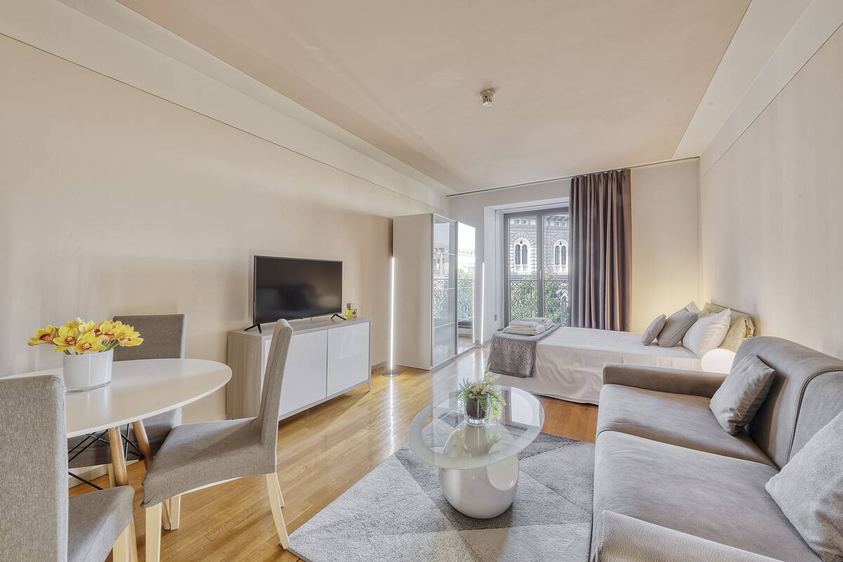 Una sala moderna con comedor, un sofá, un televisor y vistas al exterior.